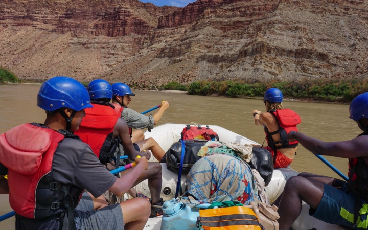 A group of people wearing safety gear navigate a raft.